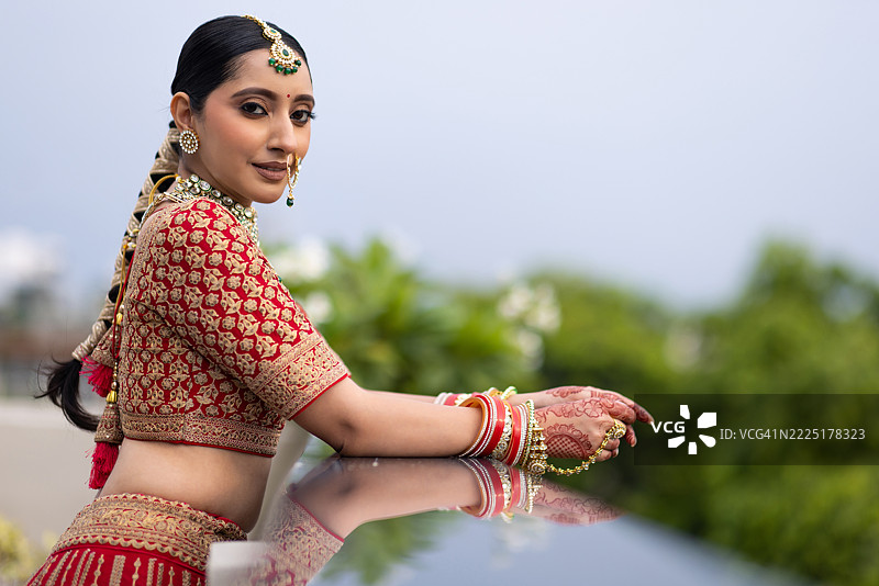 非常美丽的年轻印度新娘在户外穿着奢华的婚礼服装，化着妆，佩戴着华丽的珠宝的肖像照片图片素材