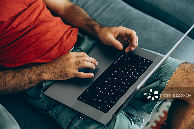 男人坐在沙发上使用笔记本电脑。图片素材