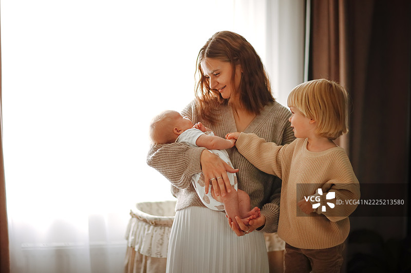 金发的哥哥在窗边与妈妈和宝宝在一起，充满温情。图片素材