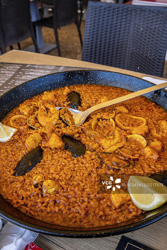 热气腾腾的西班牙海鲜饭，配有贻贝、虾和鱿鱼，盛在传统锅中，点缀着柠檬，随时可以享用。图片素材