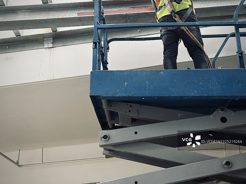 穿着安全带的升降机操作工站在剪刀升降平台上图片素材