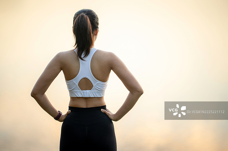 年轻亚洲女性运动员在公园里跑步的背影。女性在户外锻炼前热身，阳光明媚。健康的女性在大自然中锻炼。图片素材