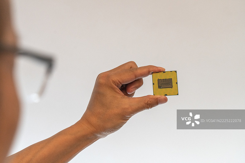 一只手在白色背景下握着一个微芯片的特写。图片素材