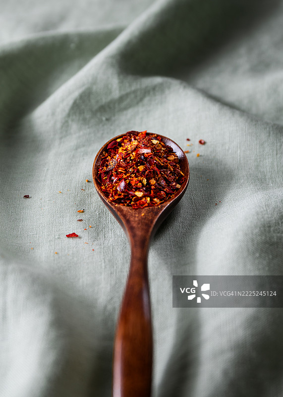 绿色布料背景上的木勺，盛满了红辣椒碎片，西班牙图片素材
