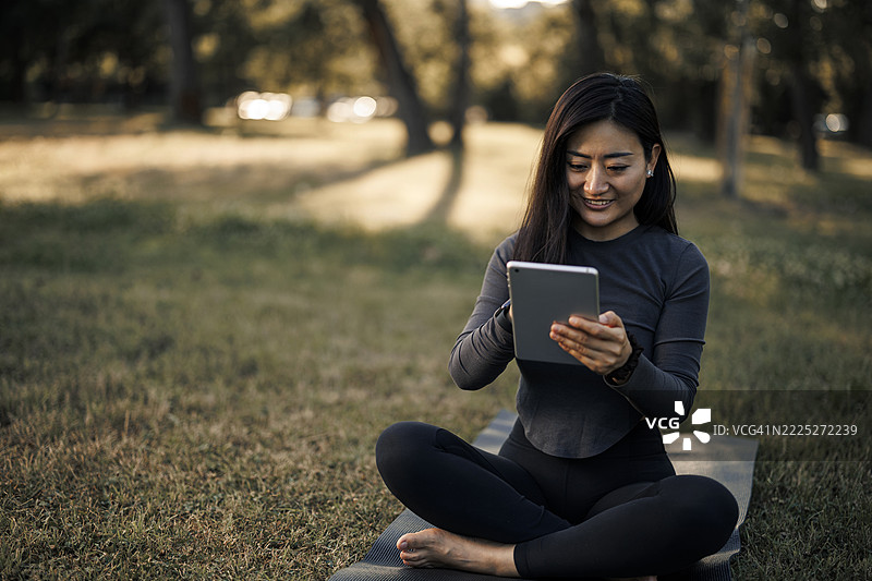 年轻的中国女性在运动垫上休息时使用平板电脑并喝水图片素材