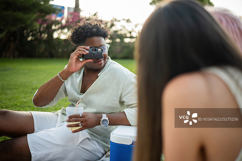 年轻男子在野餐时用一次性相机给朋友们拍照图片素材