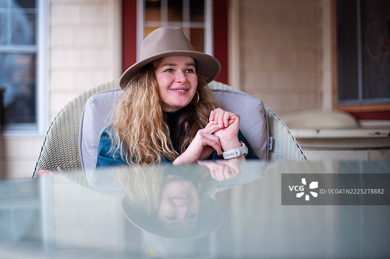 一位49岁的金发女性戴着宽边帽，享受咖啡馆露台的咖啡时光。图片素材