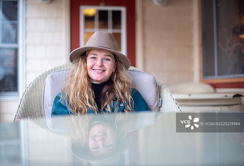 49岁的金发女性穿着时尚的米色帽子，悠闲地坐在门廊椅子上。图片素材