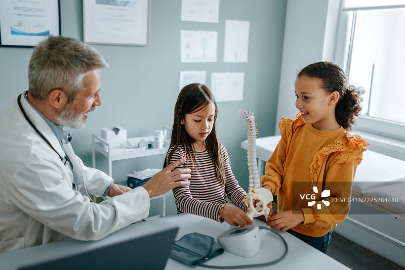 医生在医疗办公室向两个小女孩解释脊柱模型图片素材