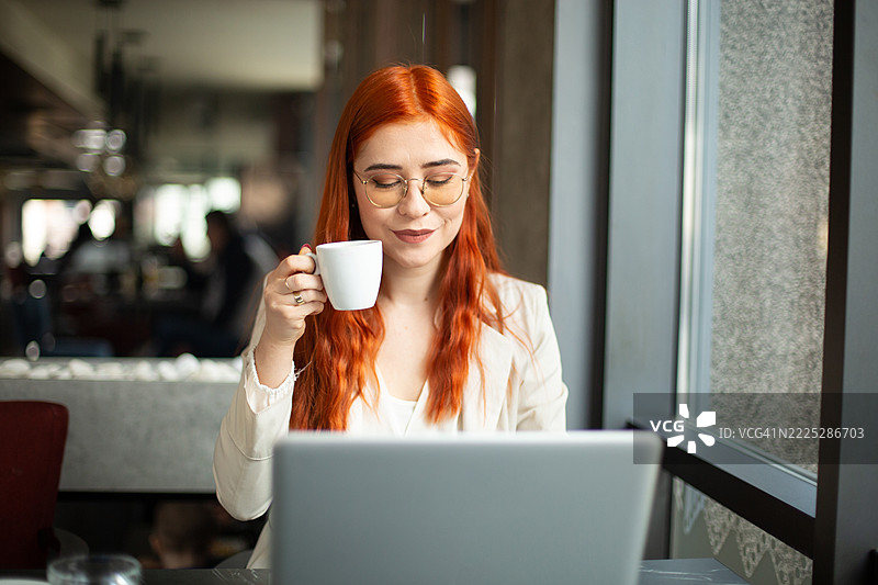 女商人在咖啡馆喝咖啡并使用笔记本电脑工作图片素材