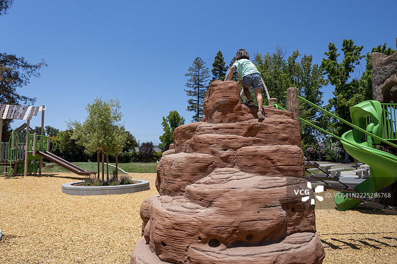 年轻的日本男孩在公园游乐场攀爬岩石结构的顶部图片素材