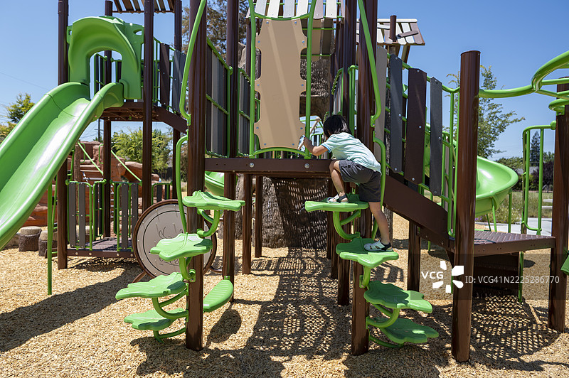 日本男孩在阳光明媚的夏日，攀爬现代户外游乐场中的大型人造树。图片素材