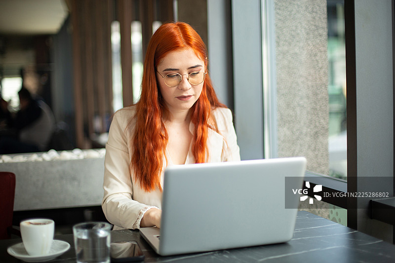 专注的女商人在咖啡馆使用笔记本电脑，享受咖啡休息时间图片素材