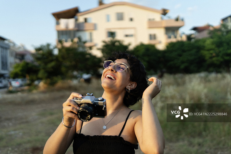 微笑的女性在金色时光的田野中用复古相机拍照图片素材