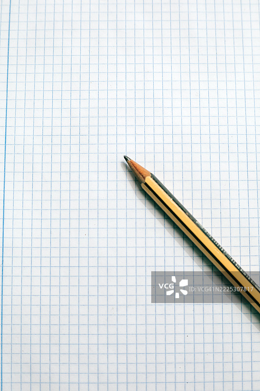 极简概念图像，展示一支铅笔静静地放在方格笔记本纸上，象征着创意、规划或学习。图片素材
