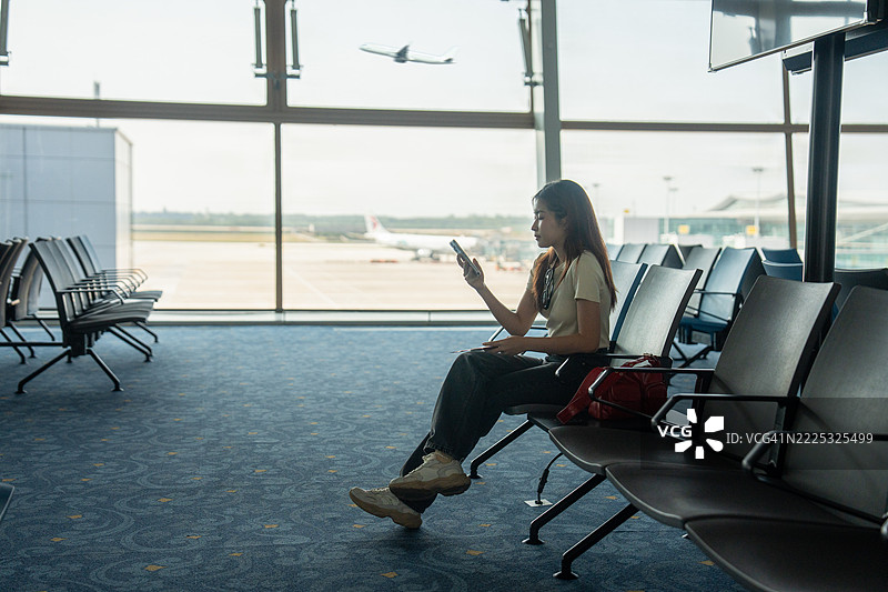 一位满意的亚洲女性在机场休息室等待航班时使用平板电脑或智能手机图片素材
