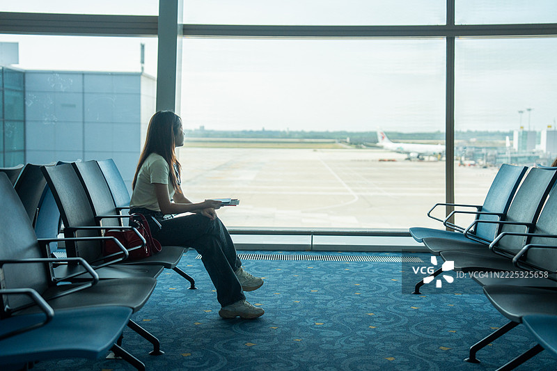 旅客们站在机场窗边，欣赏日落。在登机口等待出发时，休息室里的一位女士在观察飞机。这是一种旅行的生活方式。图片素材