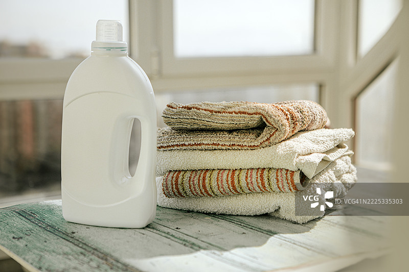 干净清新的洗衣概念，展示了一瓶柔顺剂和整齐叠放的毛巾。非常适合用于家居产品广告。图片素材