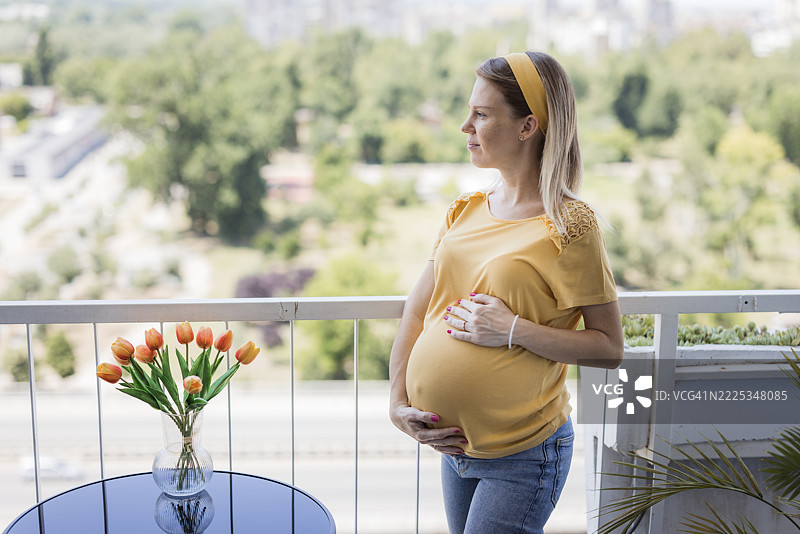 孕妇在阳台上休息，抚摸着肚子图片素材
