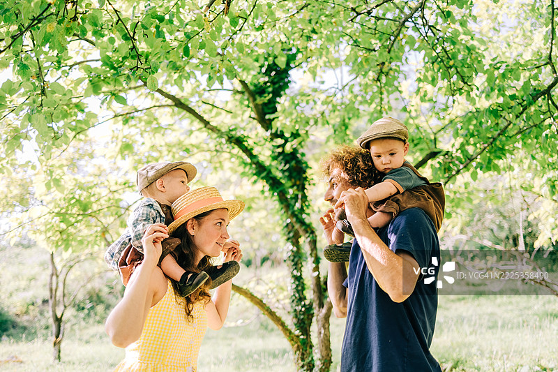 快乐的家庭在阳光明媚的绿色公园里，开心地把他们的儿子扛在肩上。图片素材