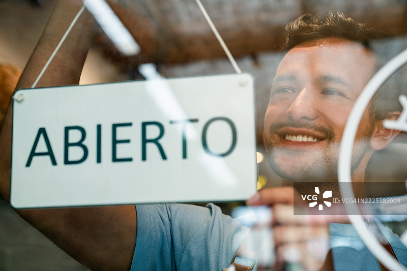 快乐的服务员在咖啡店的门上挂上开放标志图片素材