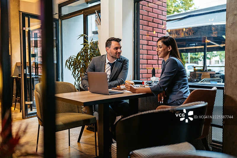 两位商务同事在餐厅享用午餐时一起使用笔记本电脑工作图片素材