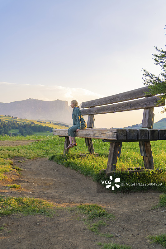 一位女士坐在一张大长椅上，眺望着宁静的山景，意大利南蒂罗尔的塞切达山，多洛米蒂山脉。图片素材