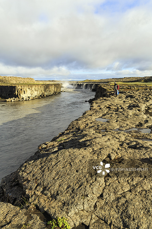 徒步者在冰岛北部约克尔萨河(Jökulsá á Fjöllum)畔,远眺峡谷、瀑布塞拉福斯(Selfoss)图片素材
