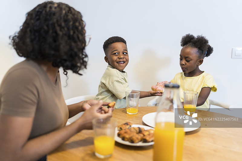 母亲和孩子们在餐桌旁享用早餐，一起分享甜甜圈和橙汁图片素材