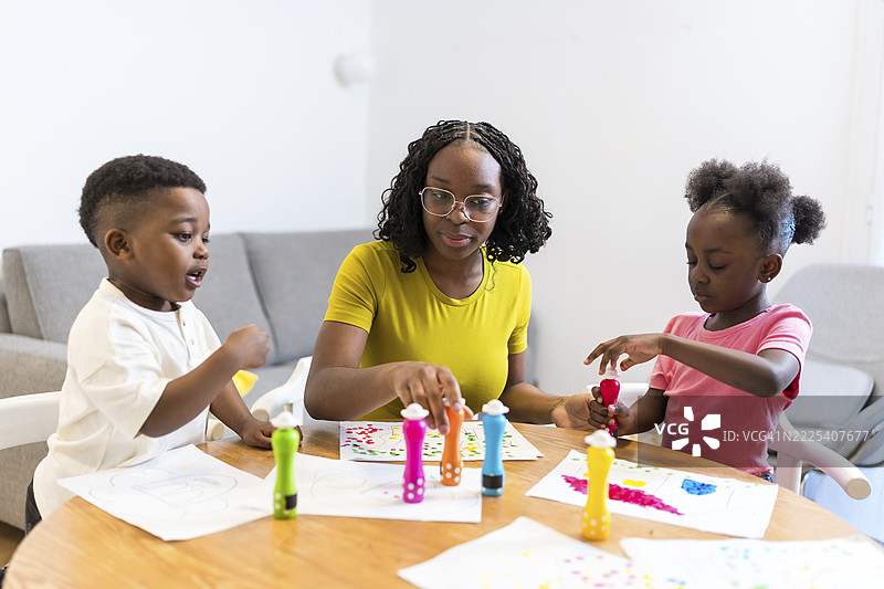 母亲和她的两个孩子在餐桌旁享受创意时光，在纸上绘制彩色圆点图片素材