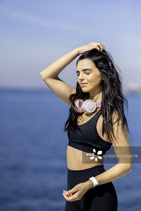 自信的年轻女性穿着运动服，在阳光明媚的海边放松。图片素材