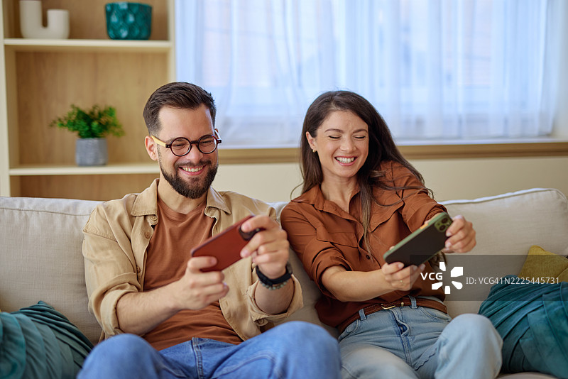 一对情侣在家里沙发上玩手机游戏，享受快乐时光。图片素材