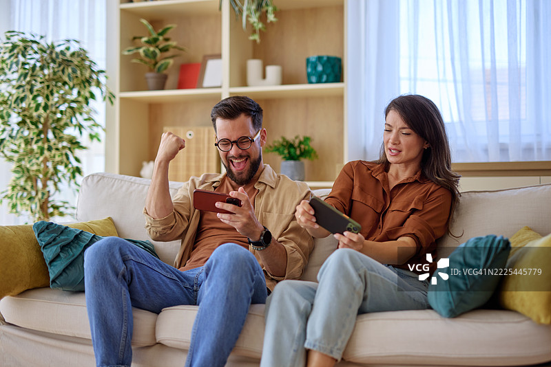 兴奋的情侣在家玩手机游戏并庆祝胜利图片素材