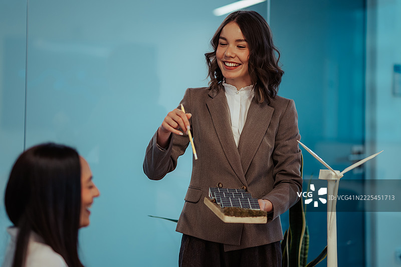 女商人在关于可再生能源的会议上向同事展示太阳能电池板模型图片素材
