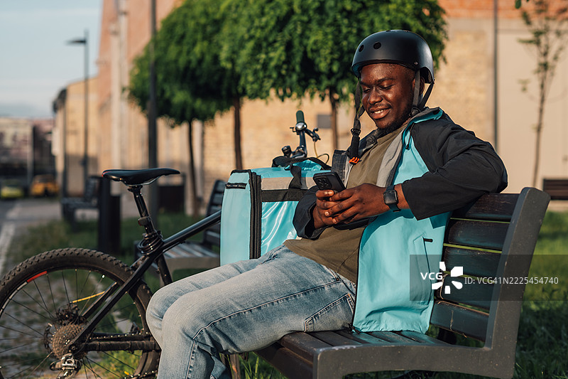 送货员坐在长椅上休息，使用智能手机应用程序图片素材