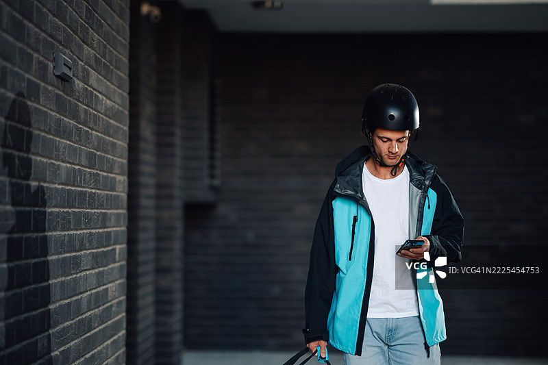 戴着头盔的快递员在砖墙旁查看智能手机图片素材