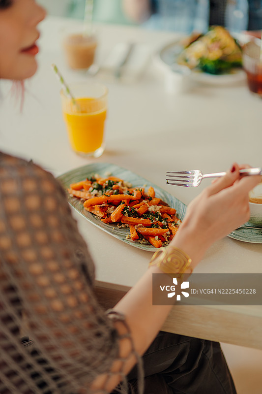女人在餐厅里吃着甜薯条，搭配香菜和橙汁图片素材