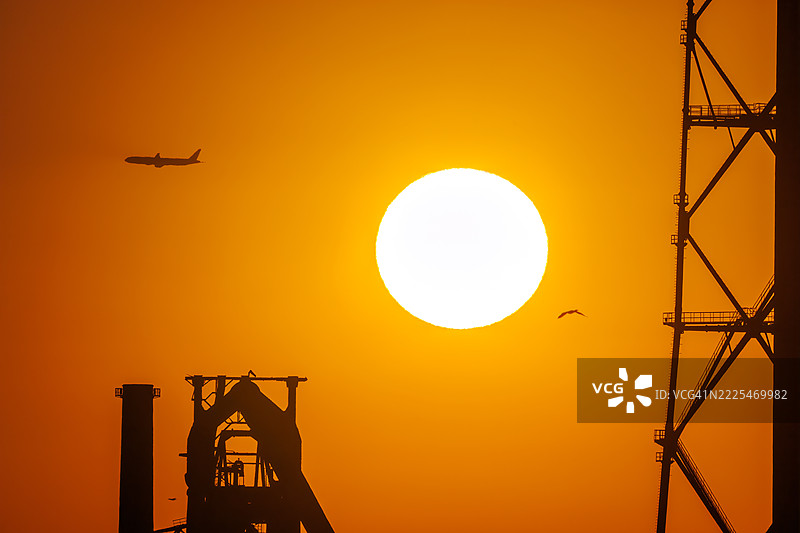 第一缕阳光与一架客机和鸟的剪影。它即将降落在附近的羽田机场。第一缕阳光从运河对岸的烟囱和电厂、钢铁厂上升。图片素材