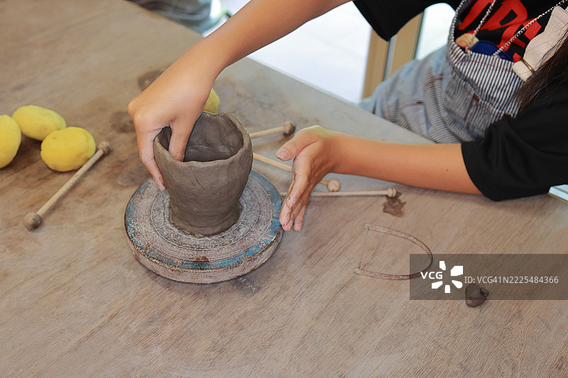 用粘土塑造梦想 一个孩子温柔的手一次次地捏造出微小的杰作。用心创作。一位年轻的艺术家在陶艺工作坊中用爱与创意塑造一个手工陶瓷杯。图片素材