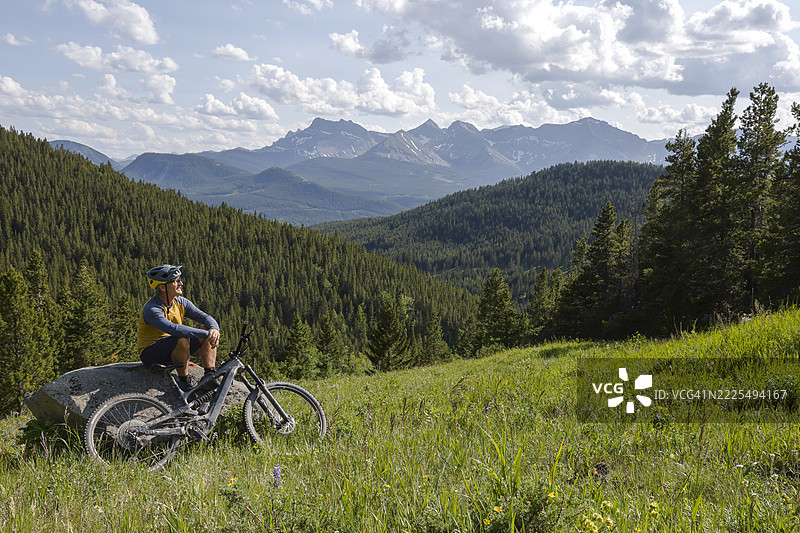 成熟男子在山间草甸上停下，骑着电动山地自行车图片素材