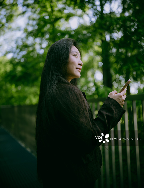 年轻自信的女商人在森林中使用智能手机。与自然连接。图片素材