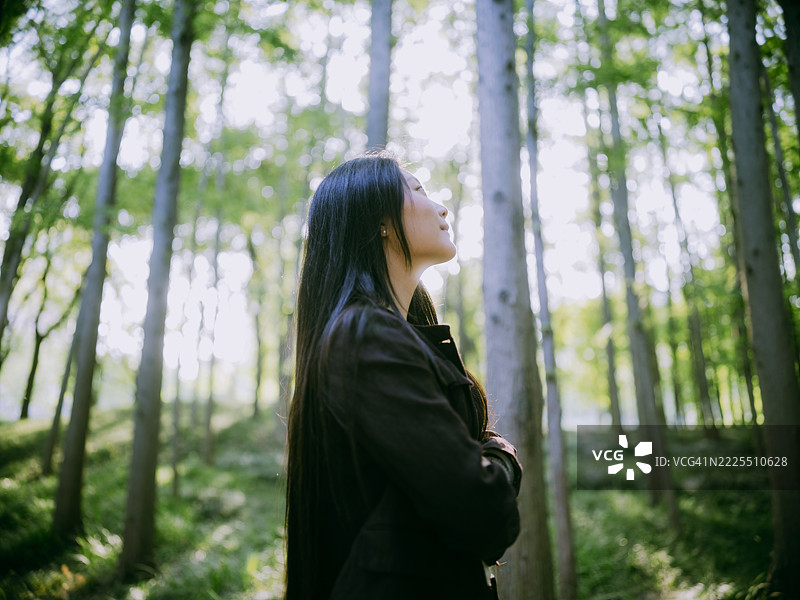 自信的亚洲女商人在森林中双臂交叉，呼吸新鲜空气，与自然亲密接触。图片素材