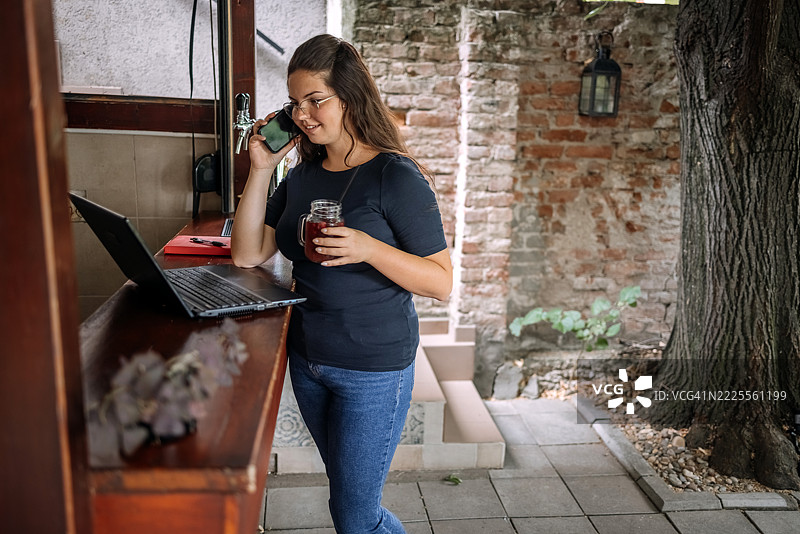 年轻女商人在咖啡馆的吧台前站着，休息时使用笔记本电脑。图片素材