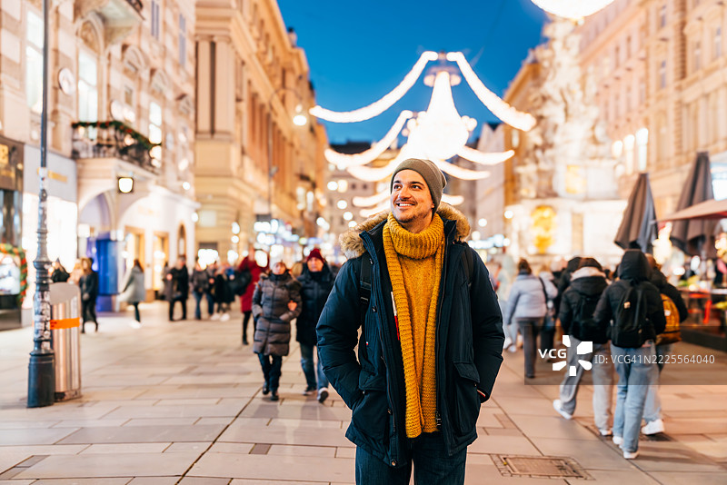 在奥地利维也纳的街道上，快乐微笑的男人被冬季的圣诞灯饰装点。图片素材