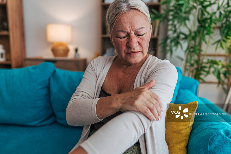 坐在沙发上的老年女性因手臂疼痛而感到不适图片素材