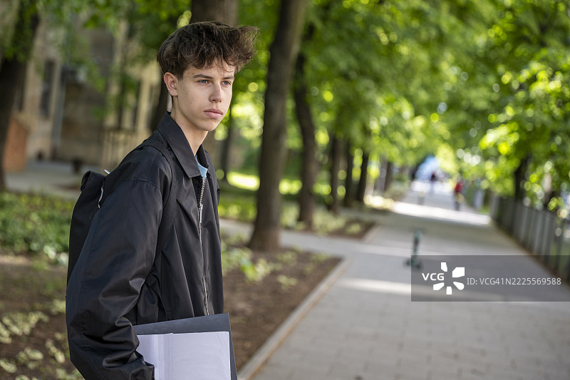 户外走着的少年男孩，手里拿着艺术作品集图片素材