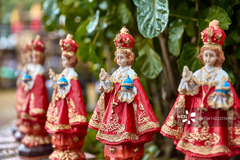 一排圣婴雕像，每个都穿着华丽的红金长袍并戴着王冠，背景是郁郁葱葱的绿叶。图片素材