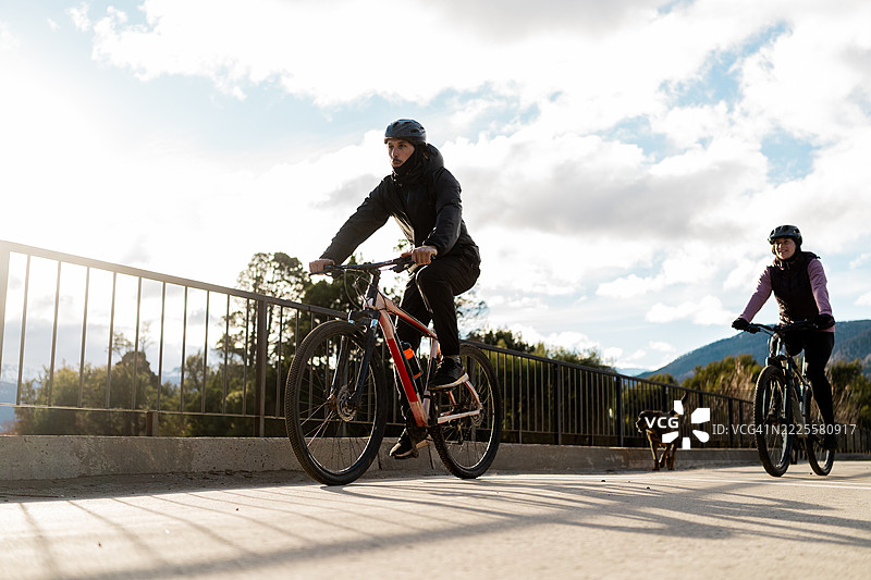 一对情侣在阿根廷巴塔哥尼亚骑自行车，身边有他们的狗。图片素材