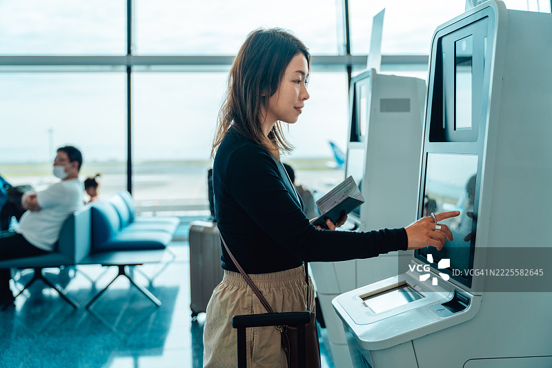 年轻的亚洲女性在机场使用自助值机 kiosks图片素材