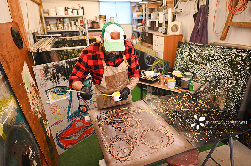 艺术家在工作室里小心地将橙色粉末颜料涂抹在金属画布上图片素材